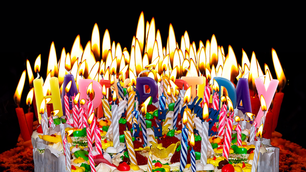 A gazillion birthday candles obscuring a cake as well as some letter-shaped candles spelling out HAPPY BIRTHDAY