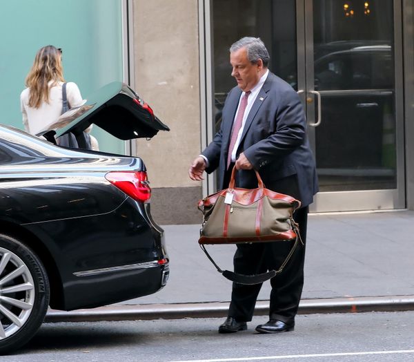 Chris Christie curbside behind a car putting some junk in the trunk