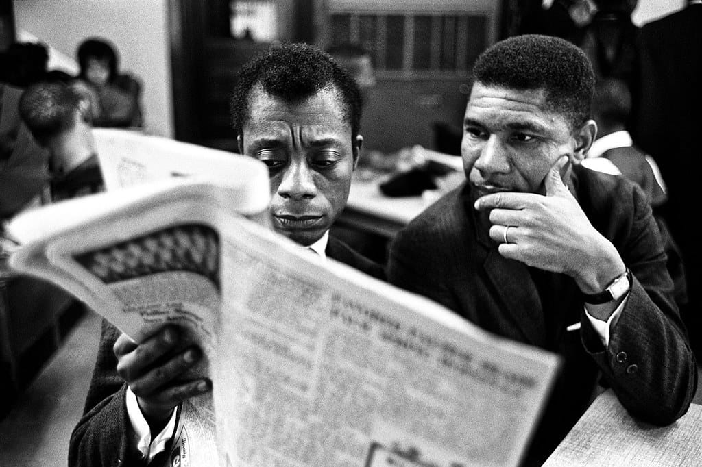 a black and white photo of james baldwin and medgar evers reading a newspaper