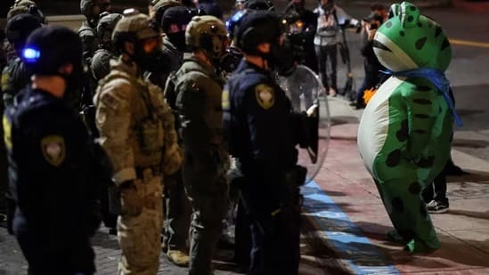 Protestor in inflatable frog costume facing down a group of armed, masked agents