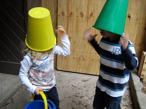 Two children wearing sand buckets as hats.