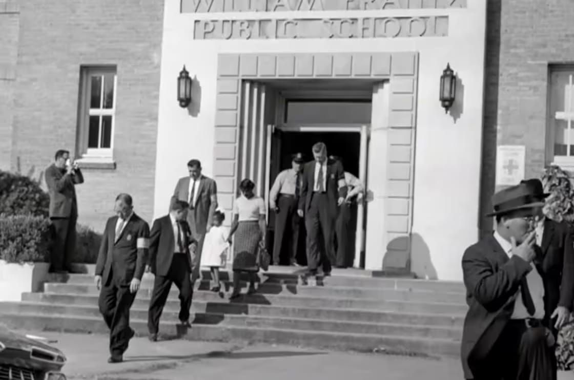 Photo of Ruby Bridges walking out of school, holding her mother's hand, surrounded by marshals