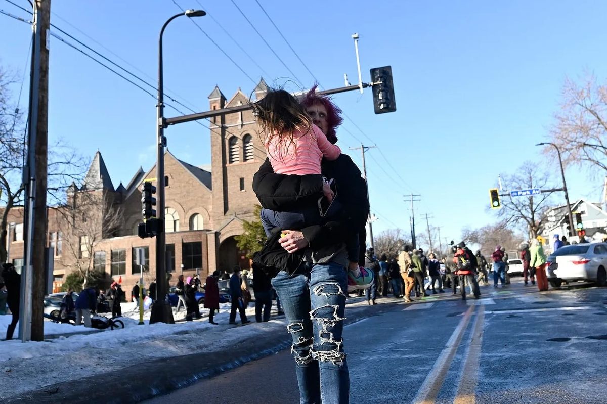Photo of a child being carried down a street away from ICE and observers, a church in the background