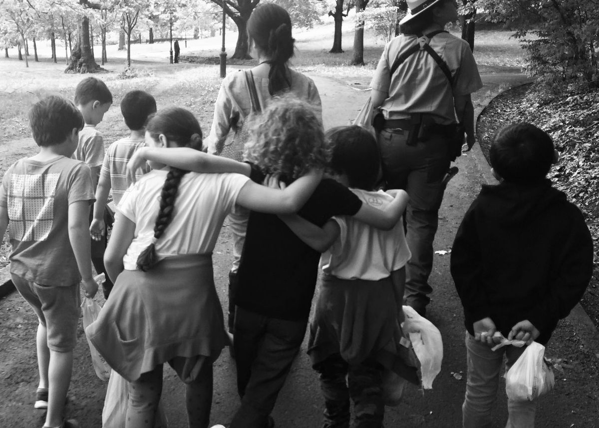 Black and white photo of a group of children arm-in-arm walking behind their teacher and a park ranger
