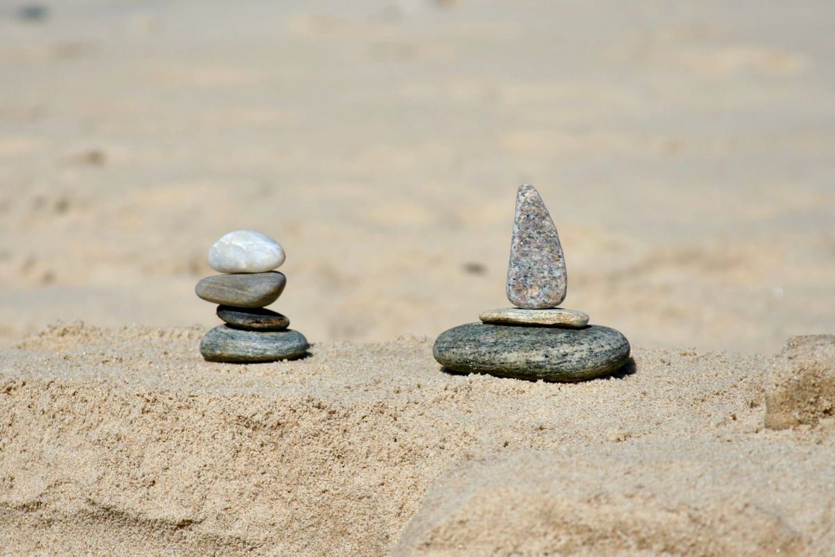 Two small stacks of stones on a sandy beach. The stones on the right form the shape of a boat.
