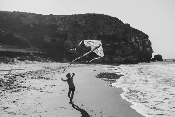 Photo of a child chasing a kite along a beach with cliffs behind him