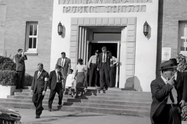 Photo of Ruby Bridges walking out of school, holding her mother's hand, surrounded by marshals