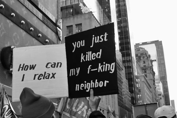Photo of a protest sign reading, "How can I relax you just killed my f—king neighbor." NYC are buildings in the background.