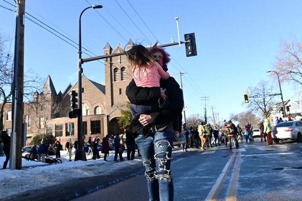 Photo of a child being carried down a street away from ICE and observers, a church in the background