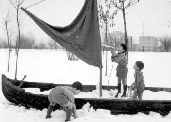 Photo of three children playing in a wooden boat with a sail erected in the center