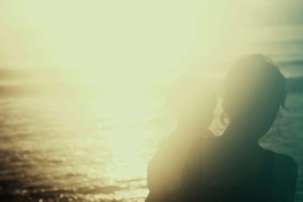 A hazy image of a woman carrying a small child. Water ripples in the sunlight beyond them.