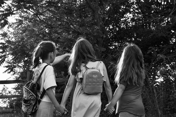 Black and white photo of three children holding hands, one child is pointing toward something unseen