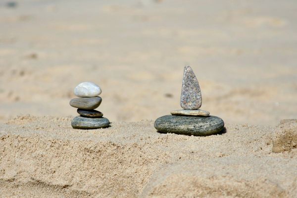 Two small stacks of stones on a sandy beach. The stones on the right form the shape of a boat.