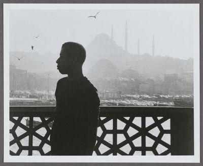 Black-and-white photograph of writer James Baldwin in dark profile silhouette, gazing left toward a hazy skyline dotted with minarets and ornate geometric railing in view.