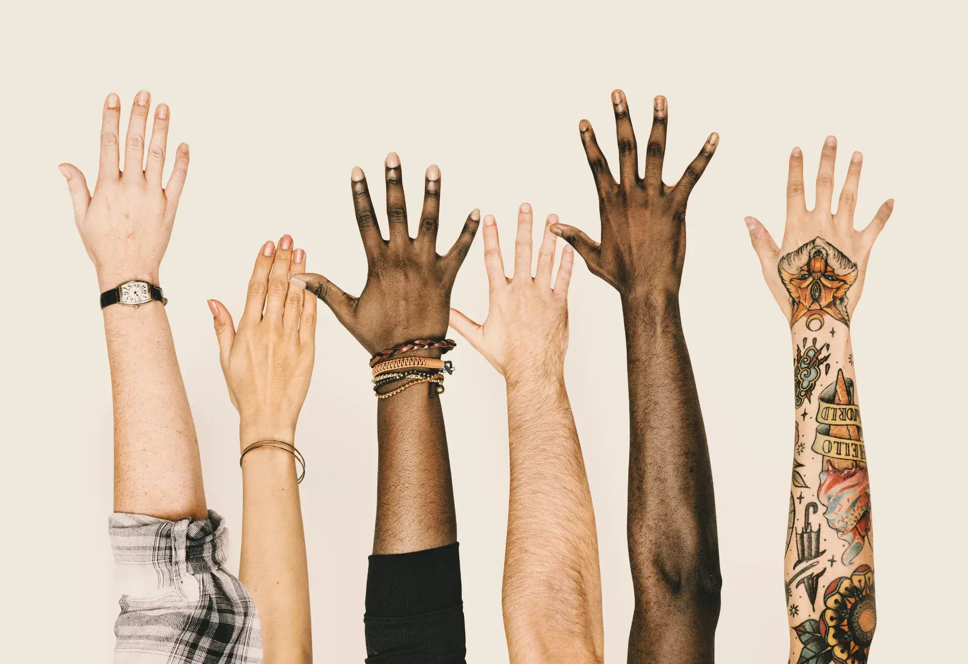 Six raised hands against a neutral background, showing a range of skin tones, tattoos, rings, and bracelets. No faces visible — just hands at the same level, each distinct.