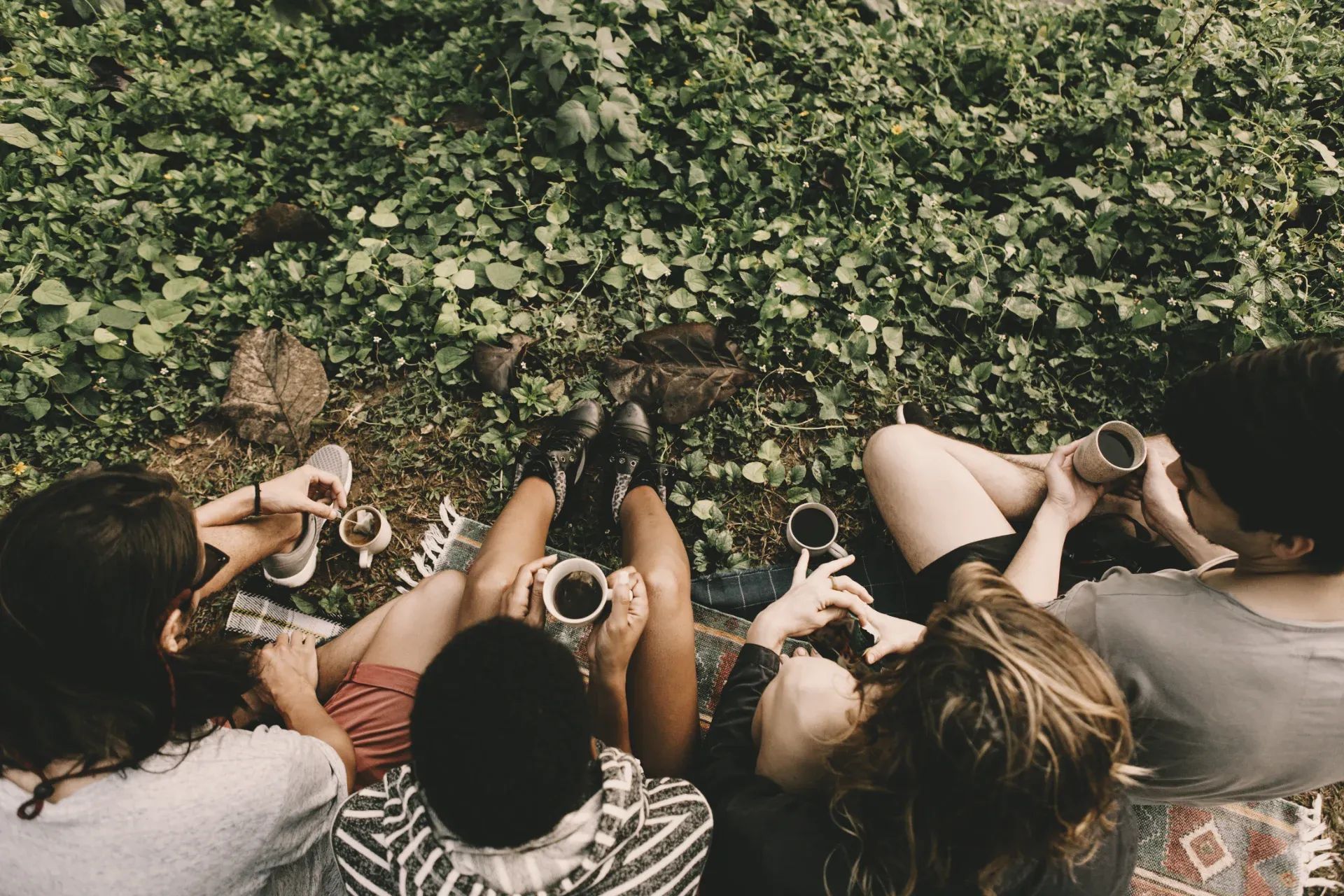 Aerial view of a group of people lying in a circle on the ground, each holding a cup of coffee. Shot from directly above — no one at the top, no one at the bottom. Equal in every direction.