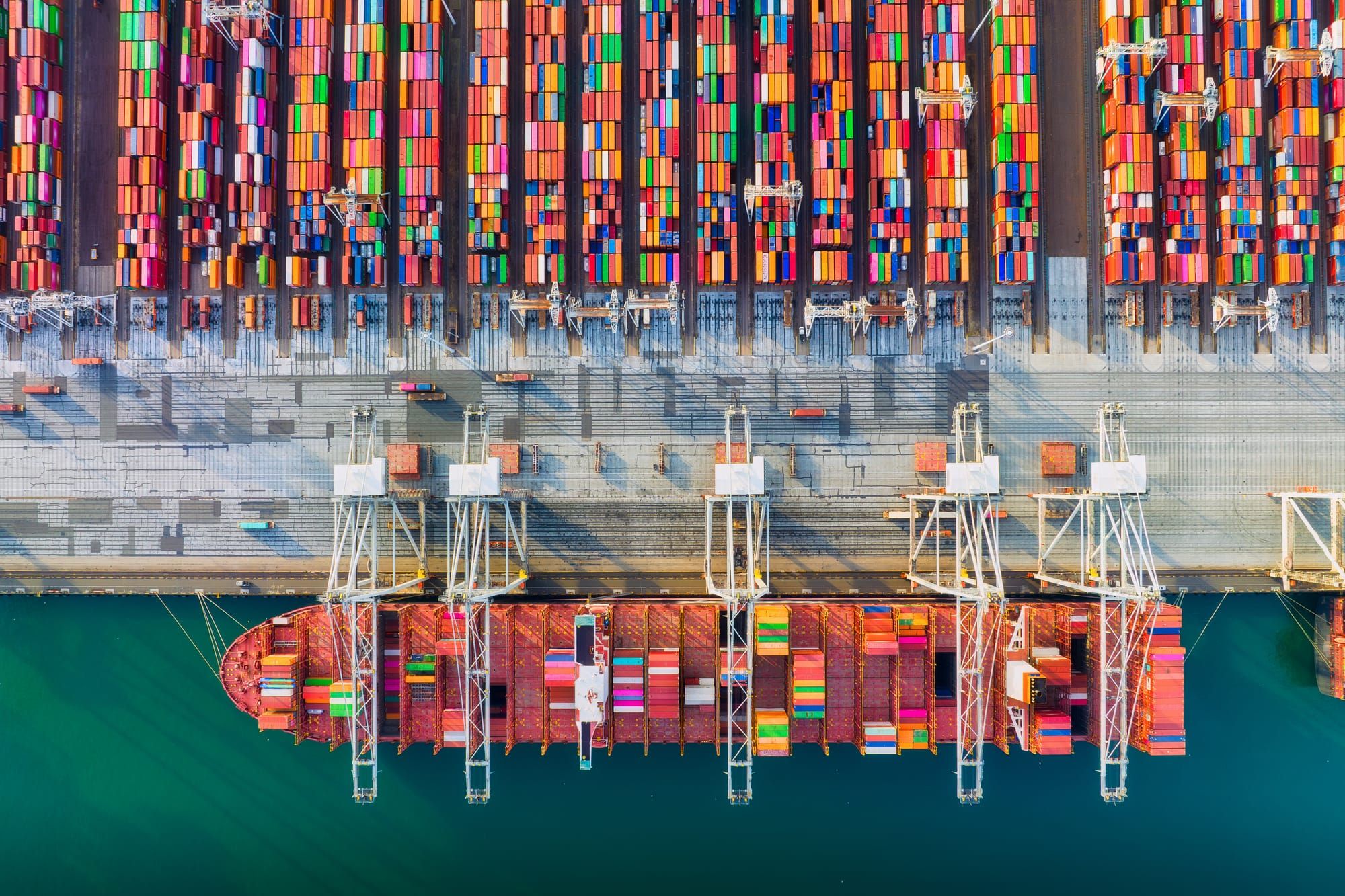 Aerial view of a cargo port with hundreds of colorful shipping containers stacked in rows along the dock.