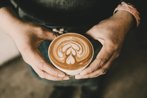 Two weathered hands cupping a latte with latte art. The hands show signs of work and wear. The coffee looks perfect. The person behind it remains unseen.