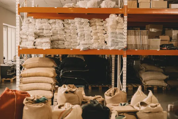 A warehouse stacked with rows of green coffee sacks and packaged bags on industrial shelving. No people visible — only the scale of the system.