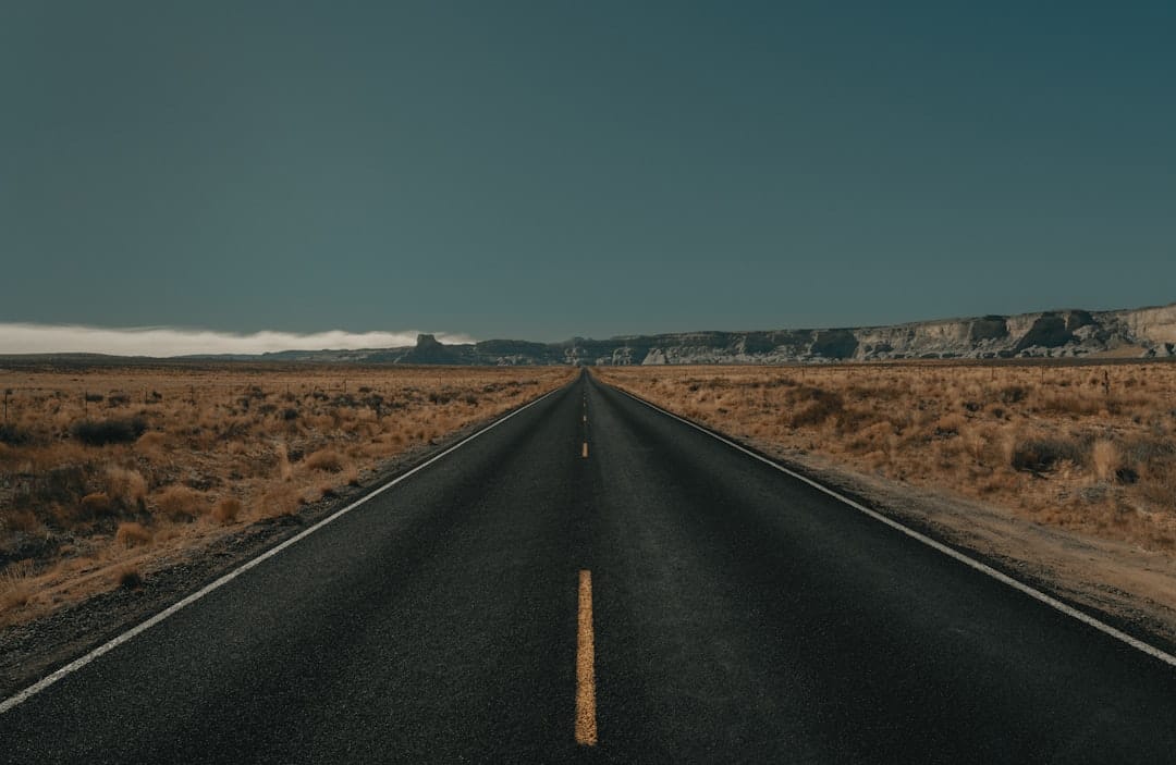 black asphalt road between brown grass field under blue sky during daytime