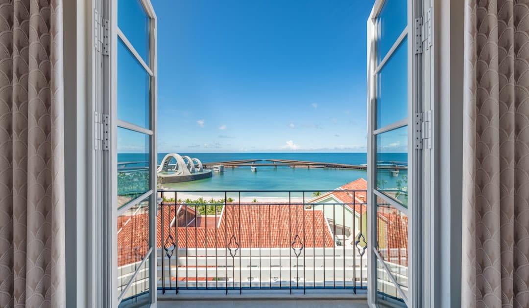 Open balcony doors reveal ocean view with tiled rooftops.