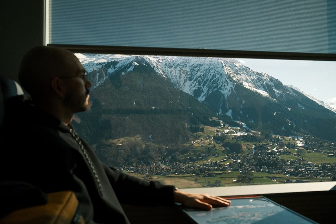Man looking out train window at snowy mountains