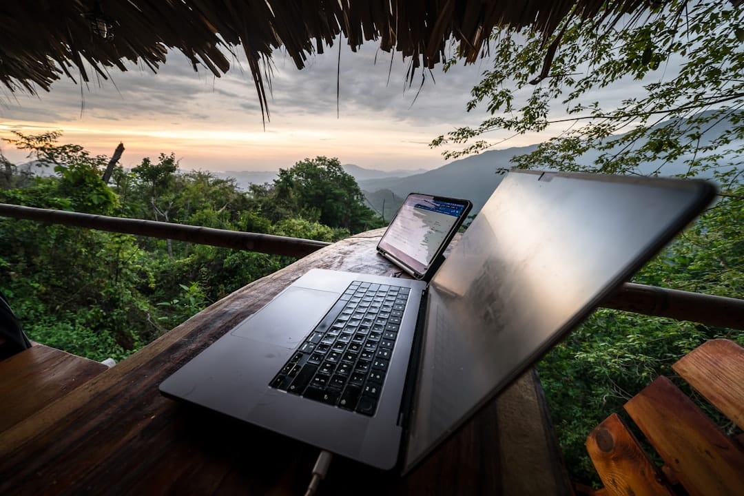 Laptop and phone on a wooden table with mountain view.