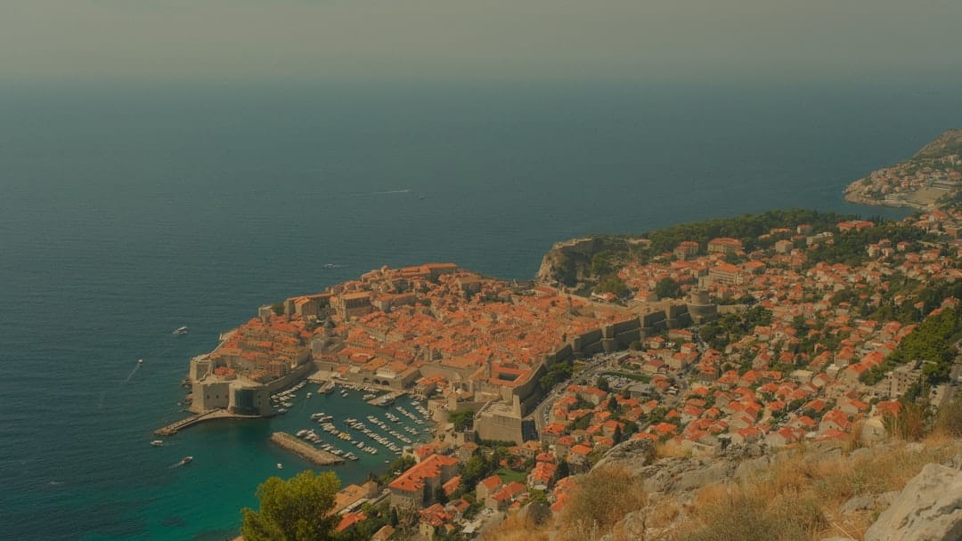 Coastal city with red roofs and harbor on blue sea