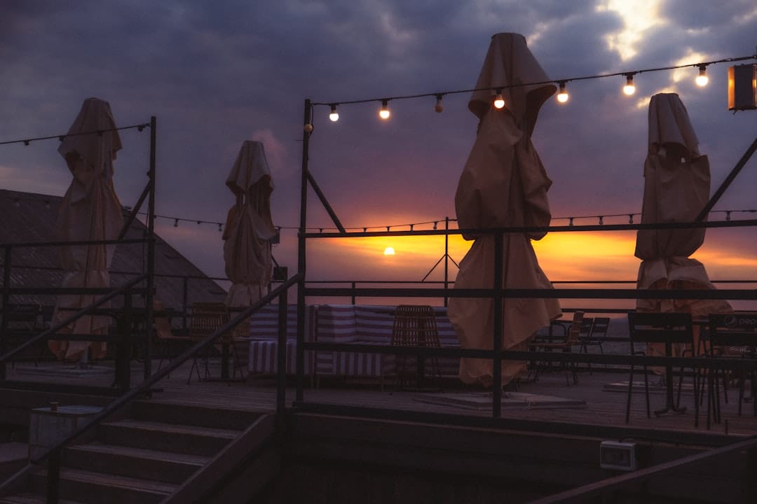 Rooftop terrace with string lights and folded umbrellas at sunset.