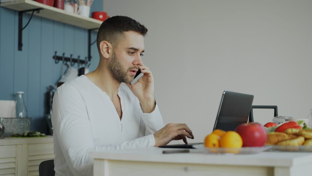 Man talking on phone while working on laptop at table