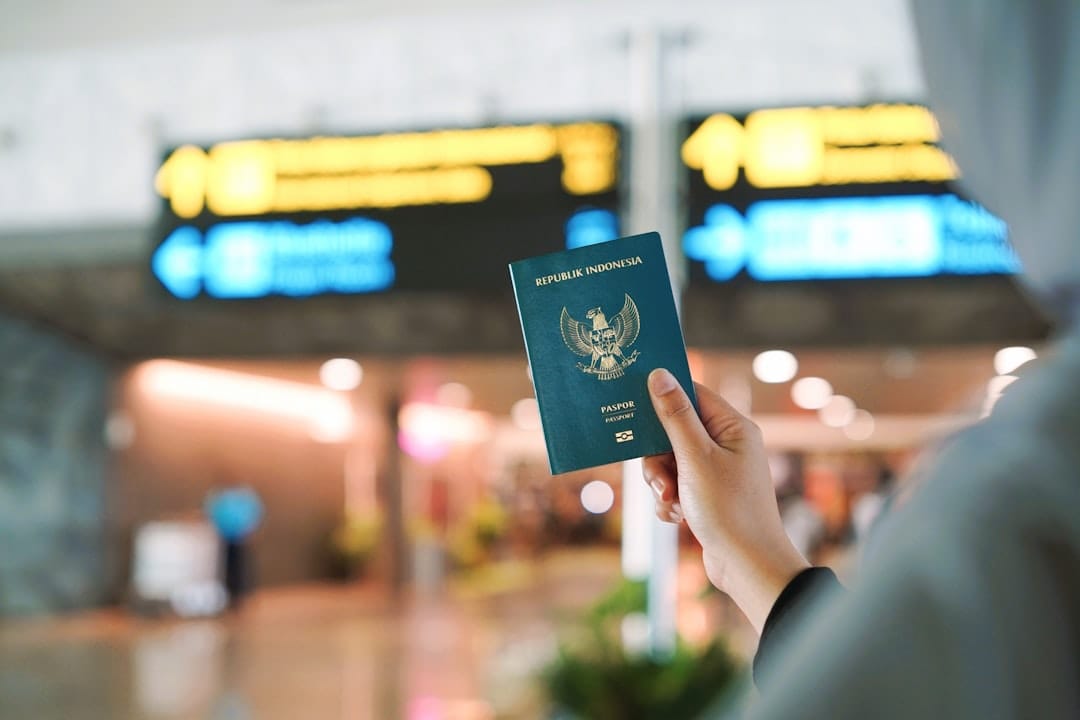 A person holding an Indonesian passport in an airport terminal with blurred signage