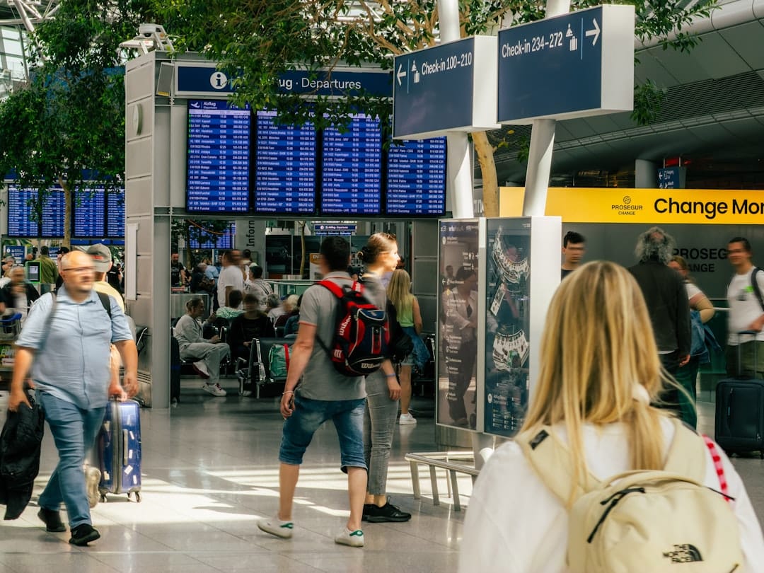 People walking through a busy airport terminal with flight departure boards and signage