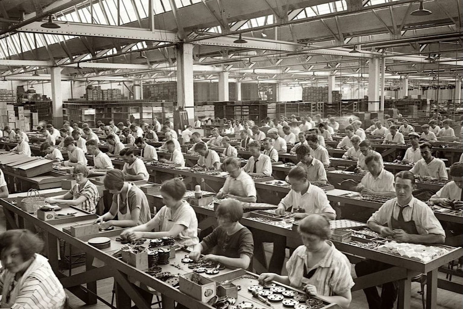Early 20th-century factory workers seated in long rows, performing precise, repetitive tasks inside an industrial hall, symbolizing discipline, order, and collective labor.