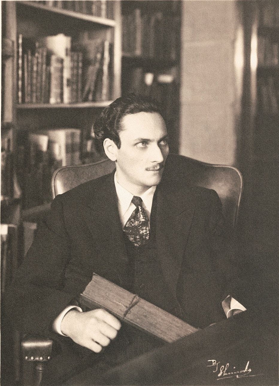 Manly P. Hall seated in his study holding a book, 1930s portrait