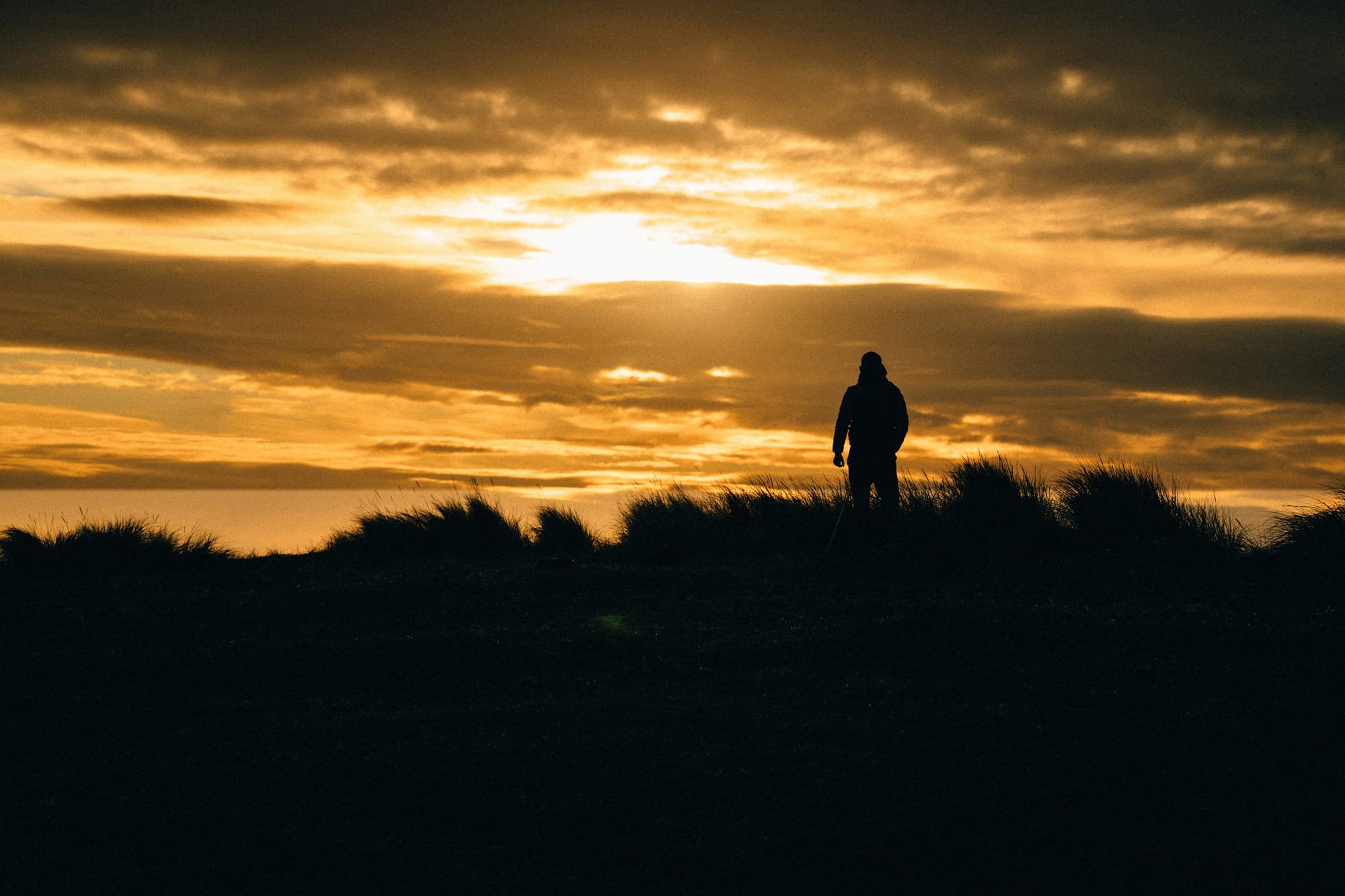Solitary figure standing on a ridge at sunset, symbolizing identity chosen privately before outcomes appear