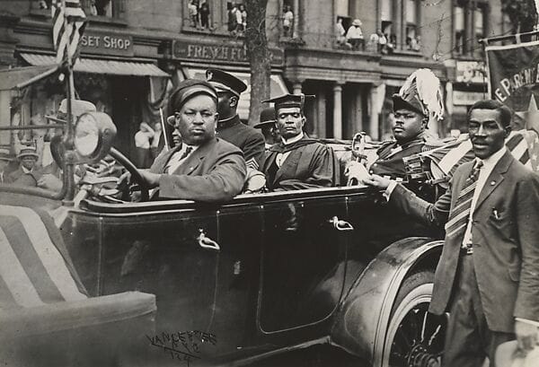 UNIA parade in Harlem during the 1920s, with crowds wearing African regalia and gathering along Lenox Avenue.