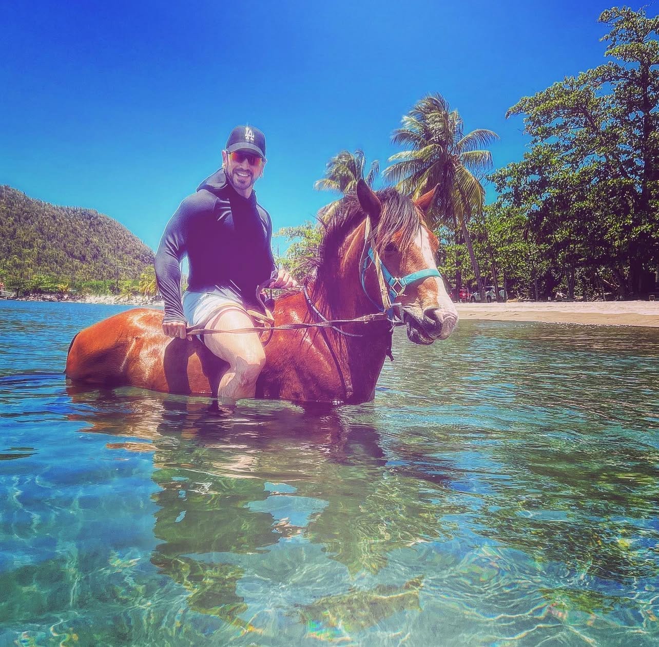 Hector Jesus Arencibia riding a horse through crystal-clear Caribbean water in Dominica, embodying the results of applied manifestation principles