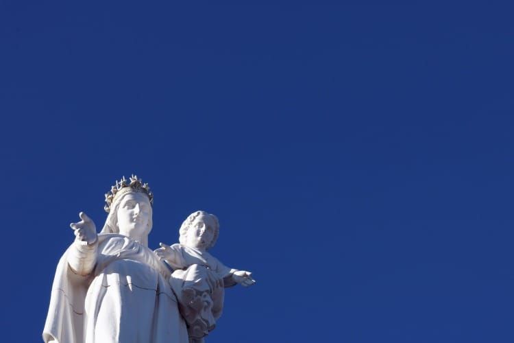 Statue of the Virgin Mary holding the Christ child against a clear blue sky — symbol of compassion and the Divine Feminine.