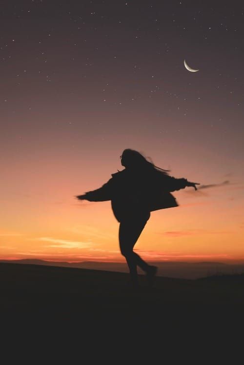 Woman with arms open wide under a crescent moon, embracing manifestation energy.