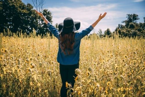Woman with arms open, allowing the sunshine in a sunflower field — Art of Allowing, Law of Attraction