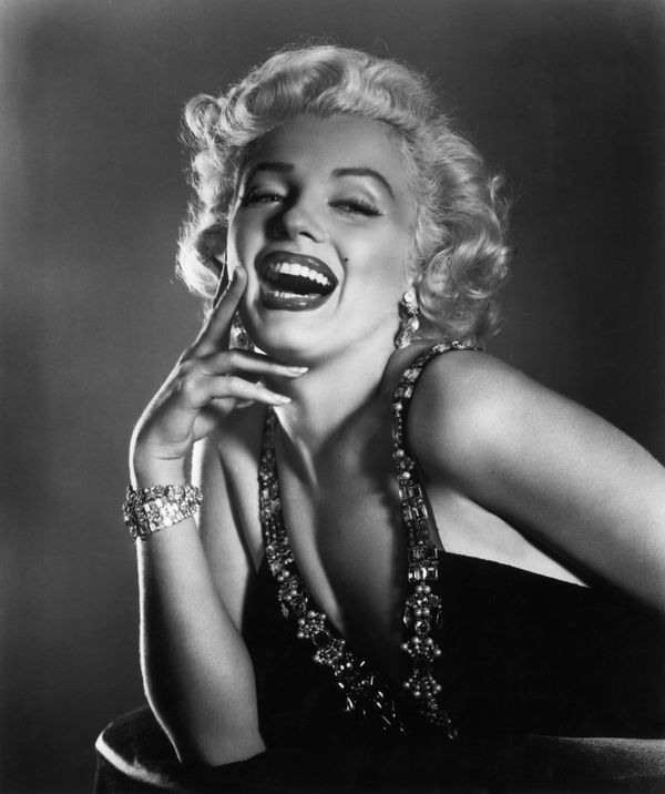 Marilyn Monroe laughing in a black-and-white 1950s studio portrait, wearing a rhinestone-strapped gown and matching bracelet