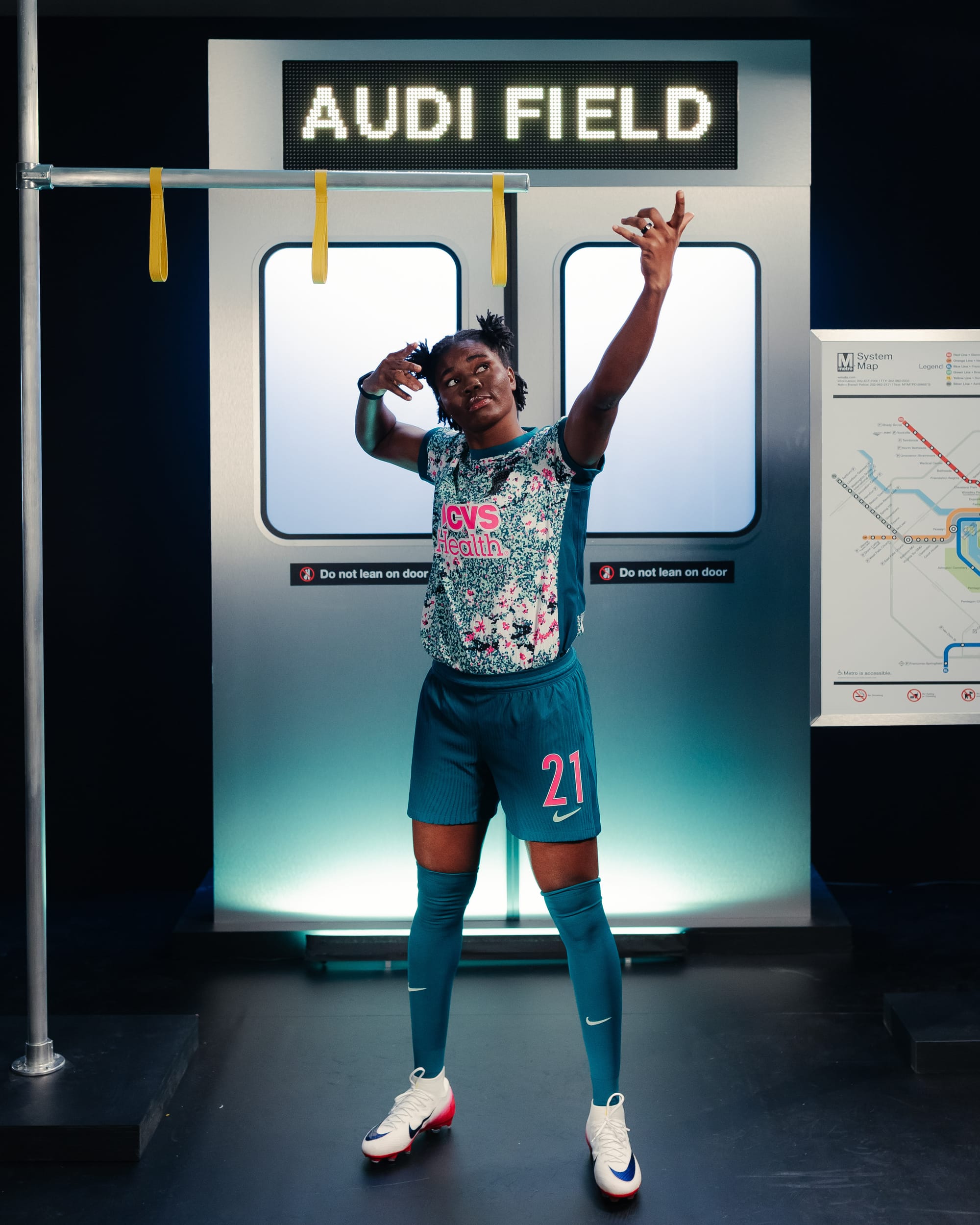 Gift Monday holds her celebratory arrow-shooting pose while wearing the full "Spirit in Bloom" kit. The shorts are solid dark green with pink numbers and a mint green Nike logo, while the socks are solid dark green with the same mint green Nike logo.