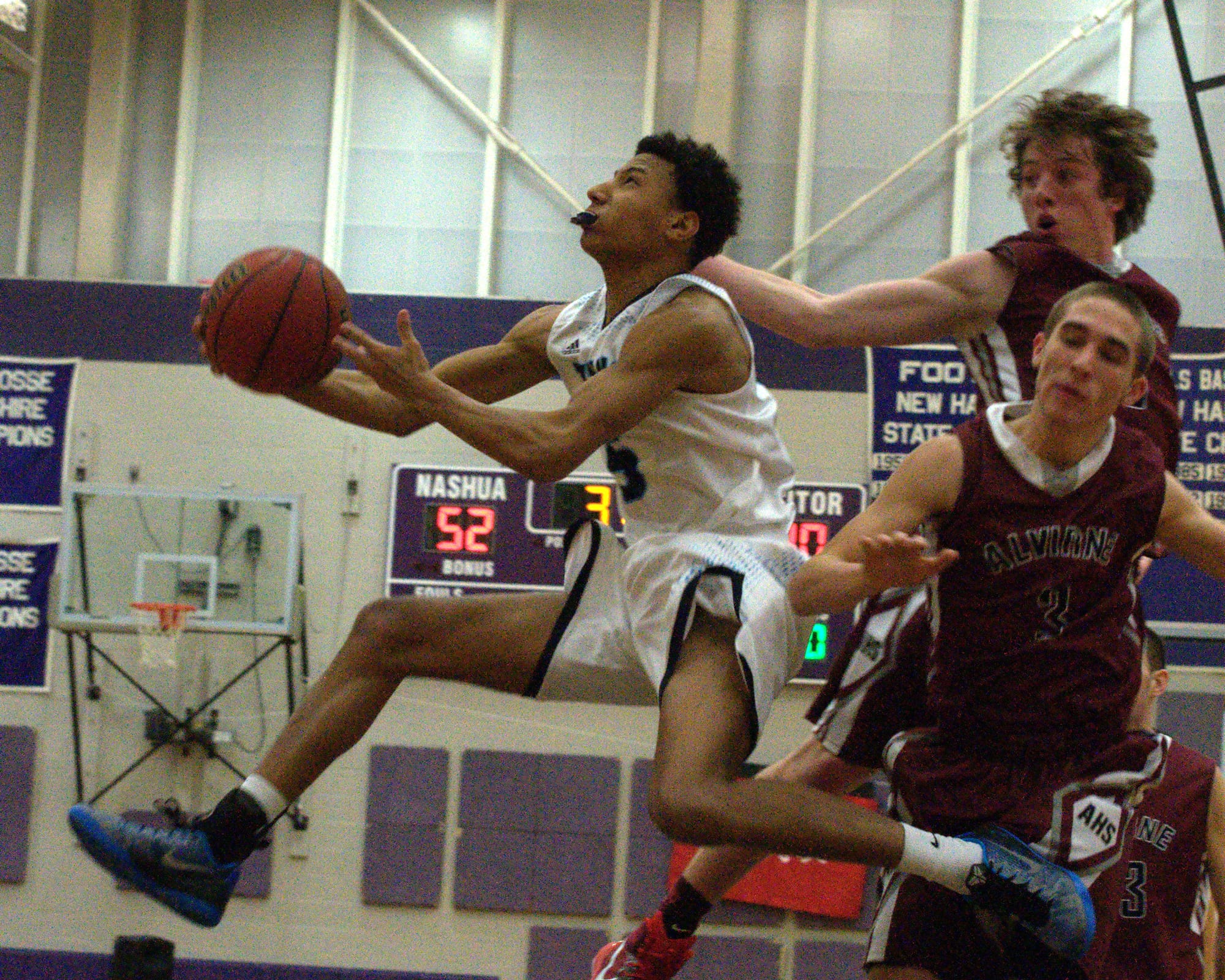 Nashua North's Brandon Rodriguez glides past Alvirne's Dan Tucci and George Notini on his way to the basket during Tuesday's game.