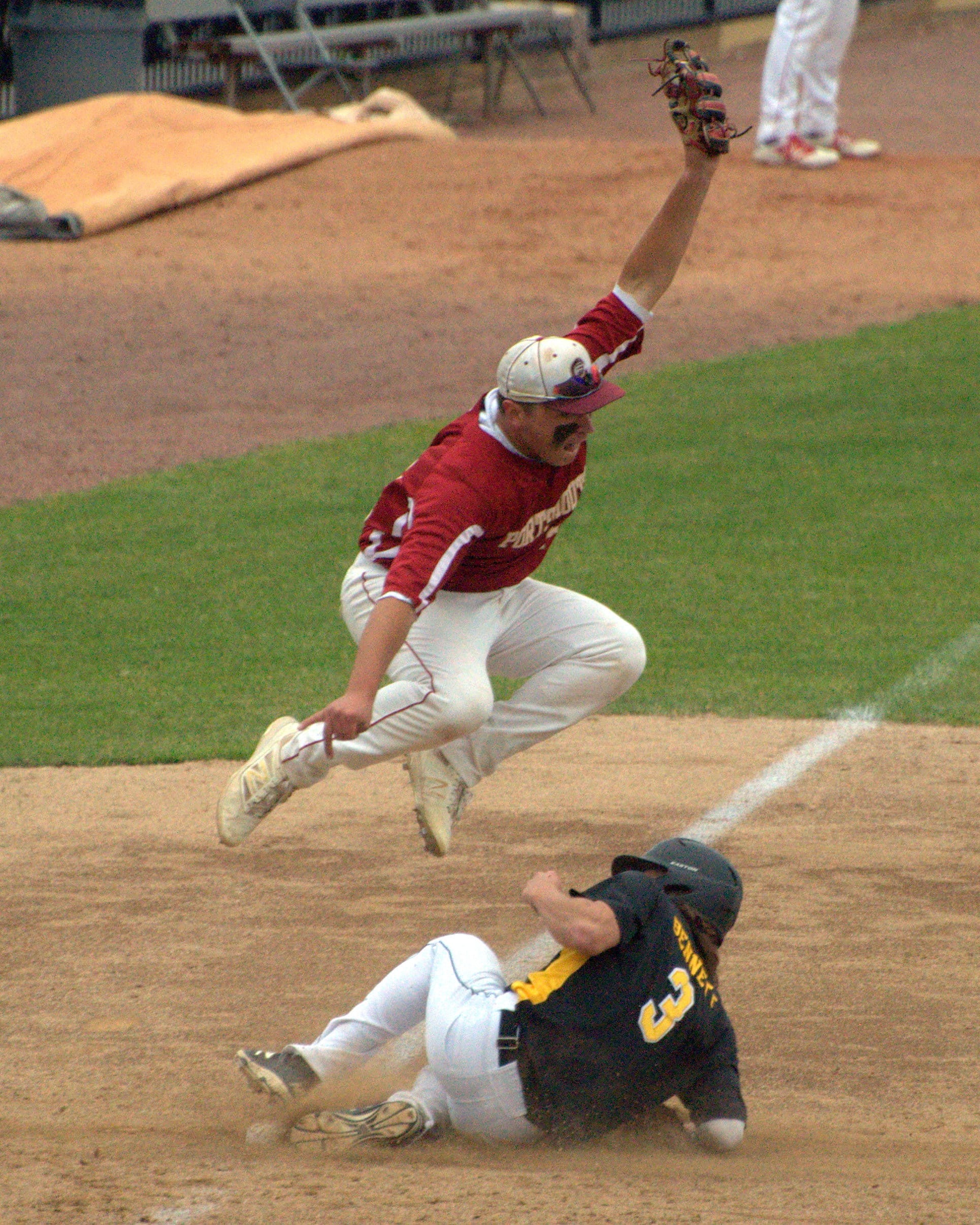 Souhegan's Thomas Bennett slides into third as Portsmouth's Josh Saurman goes up for the ball.