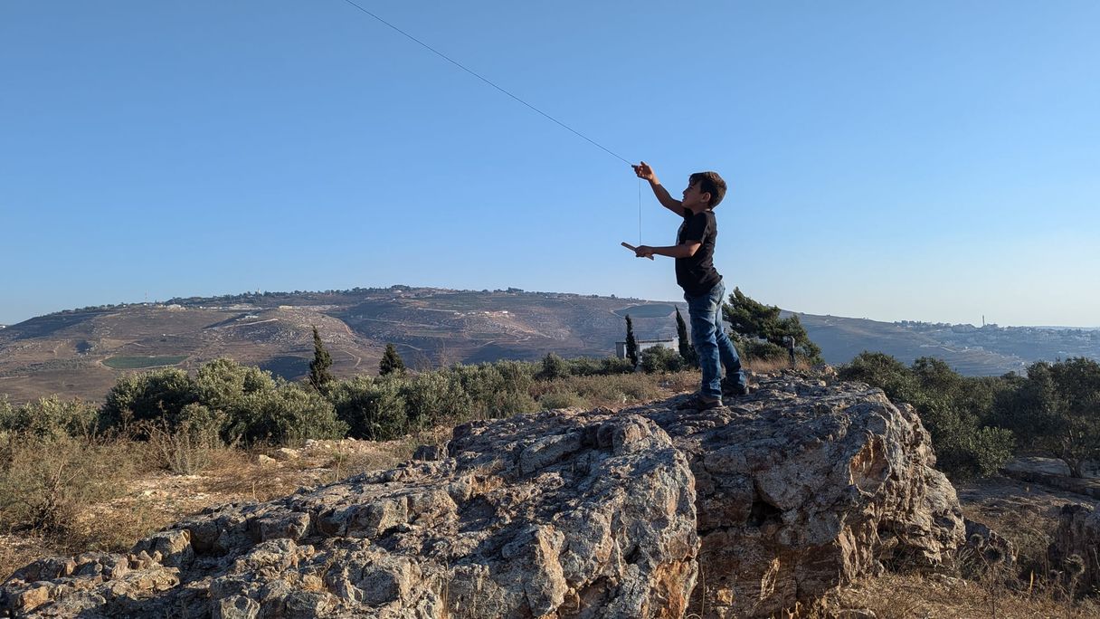 Child on top of a rock plays with a Kite