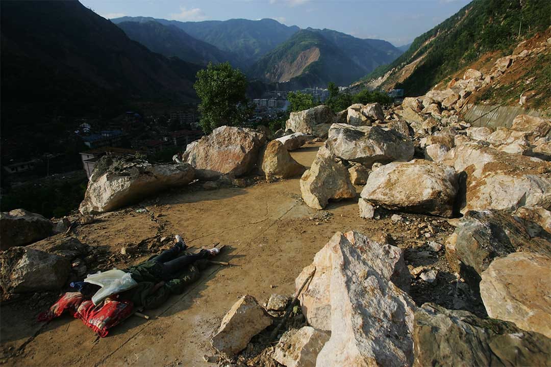2008年5月14日，绵阳市山路上一名罹难者的尸体被大石块覆盖。