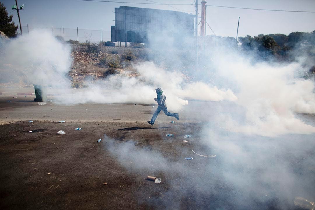 以色列，以色列防暴警察發射催淚彈，一名男生在煙霧中逃跑。