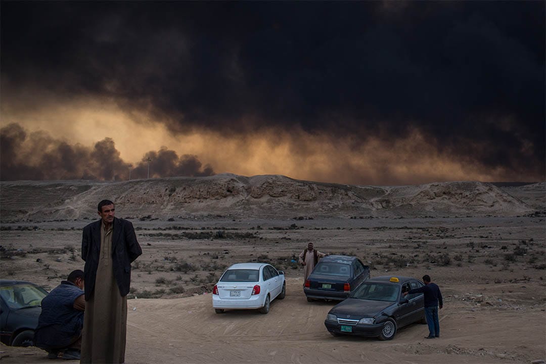 2016年11月9日，伊拉克蓋亞拉，人們站在起火的油井附近。