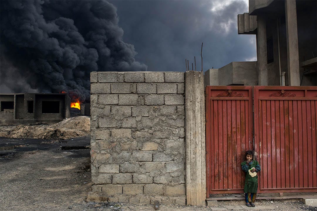 2016年11月10日，伊拉克蓋亞拉，起火的油井附近，一個女孩站在家門外吃麵包。 