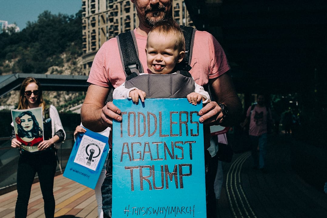 在澳門，一名父親帶同幼兒參與示威，並手持「幼兒反對特朗普」標語牌。